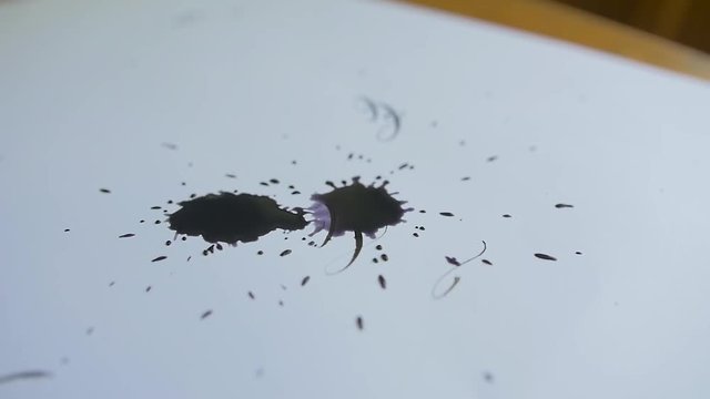 Wet ink droplets falling onto a white sheet of paper.