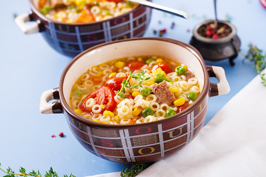 Soup with small pasta, vegetables and pieces of meat in  bowl on  blue table. Italian food.