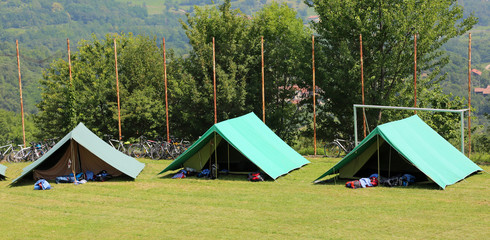 three green tents mounted by scouts in a meadow