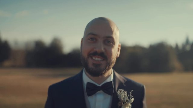 Portrait of Elegant Man smiling at camera dressed with a classy smoking and papillon, slow motion of a smile at sunset