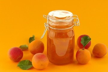 Apricot jam in a glass jar and fresh apricots on a bright orange background.Fruit preserves. Apricot dessert