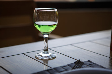 Green drink in the glass is on a wooden table. Mojito, tarragon lemonade, incomplete glass, green lemonade glows in the light