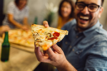 Close shot of young man with glasses holding slice of pizza