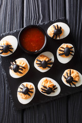 Halloween appetizer deviled eggs stuffed with mustard and decorated with olive spiders and cobweb close-up. Vertical top view