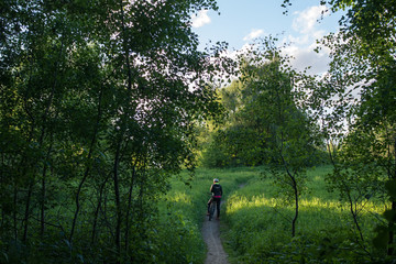 Photo from back of woman bicyclist wearing helmet riding along road in woods