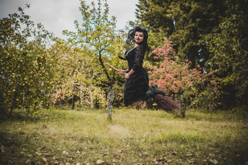Young beautiful and mysterious Witch woman Flying on the Broom in woods. Levitation, a witch in a hat flies on a broom, free space. Halloween holiday, magic