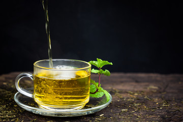Cup of hot tea and mint herb on wood background .
