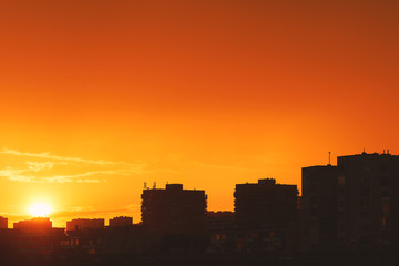 Fototapeta na wymiar Bright orange sunset over the evening city. Bright lights of tall buildings of urban buildings. Great disk of the rising sun. Sun rays