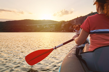 A red-haired young woman rowing on an inflatable kayak on a lake among beautiful mountains against...