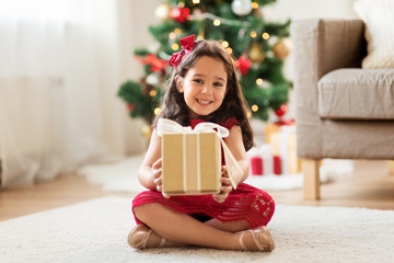 christmas, holidays and childhood concept - happy girl with gift box at home
