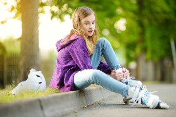 Pretty little girl learning to roller skate on summer day in a park. Child wearing safety helmet...