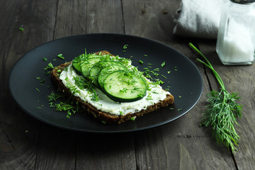 Slice of dense rye bread with cream cheese, cucumber and dill