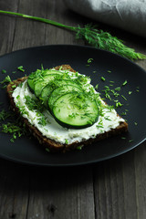 Slice of dense rye bread with cream cheese, cucumber and dill
