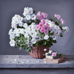 Still life with white and pink roses in basket and books on wooden table