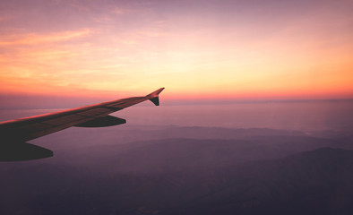 Airplane wings in the sky and a mountains view scene in the sunrise. Travel and adventure.