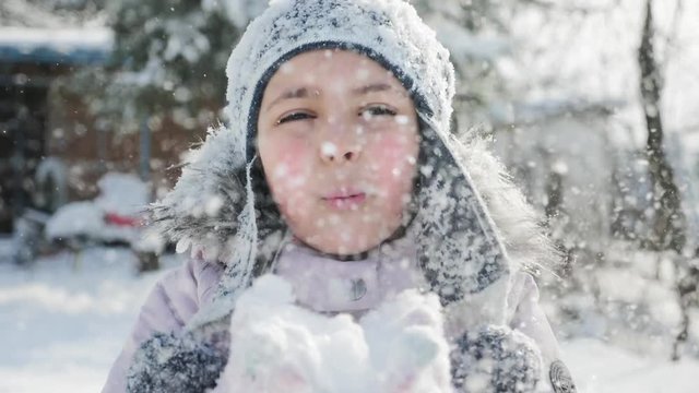 Blowing snow. Beauty joyful teenage small girl having fun in winter park. Beautiful girl blowing snow and smiling outdoors. Enjoying nature. Slow motion video footage