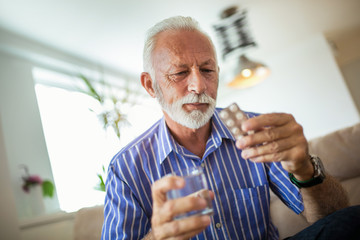 Senior man taking pills at home - Powered by Adobe