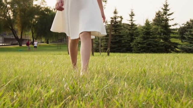 Beautiful little girl goes barefoot on grass in sunny summer park