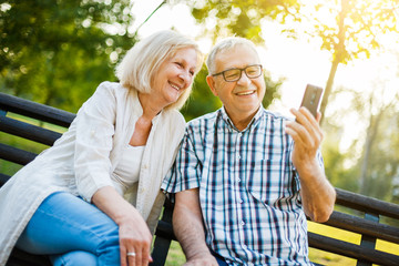 Happy senior couple is using smartphone in park.  - Powered by Adobe