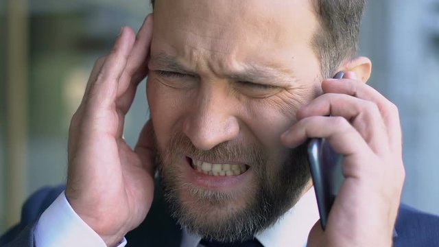 Middle-aged boss suffering from migraine, talking on phone, headache close-up