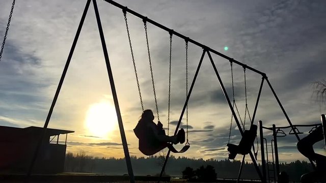 Slow motion silhouette of a child on a swing.