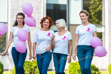 happy women holding pink balloons and walking together, breast cancer awareness concept