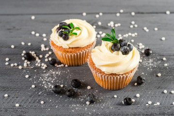Creamy cupcakes with blueberries on the wooden background