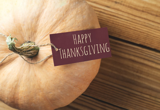 Happy thanksgiving with pumpkin on wooden table and greeting inscription on paper