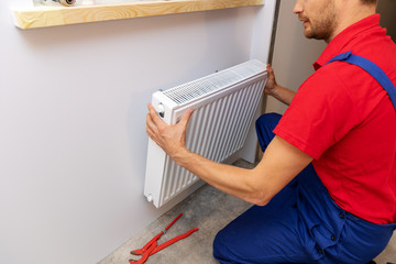 plumbing services - plumber installing heating radiator on the wall
