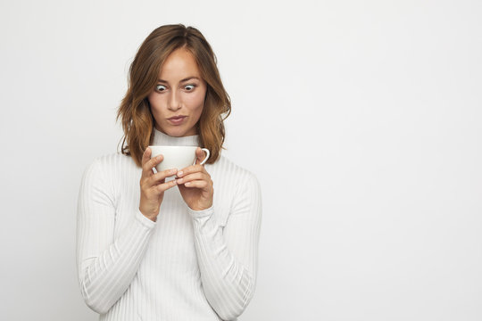 young woman with cup of coffee looks down funny