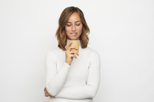 young woman with cup of coffee looks down bites the lip