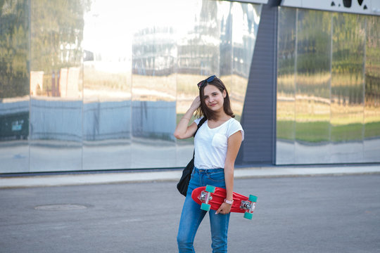 A nice girl with a skateboard in her hands looks at the camera and smiles on a gray background. Modern leisure for teenagers. sport