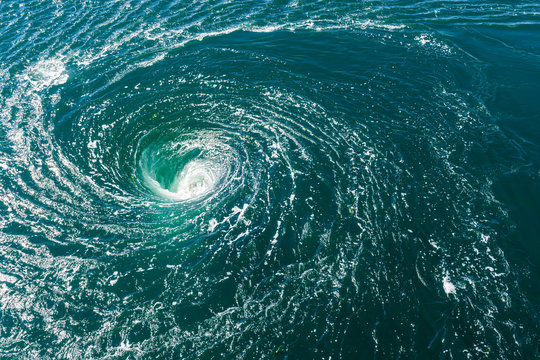 High angle view of a powerful whirlpool at the surface of green water with foam.