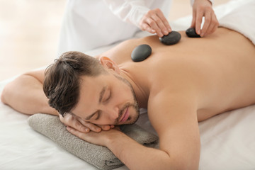 Obraz na płótnie Canvas Handsome man having stone massage in spa salon