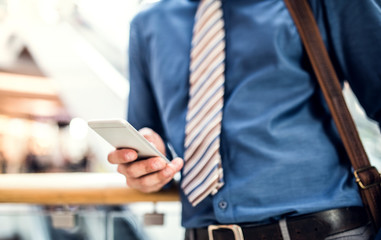 A young businessman with smartphone walking in a modern building, texting.