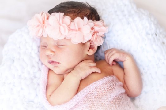 Cute sleeping newborn Caucasian baby girl a pink flower head bow. Sweet infant girl in her sleep. A classical newborn infant photo session. First days of her life concept
