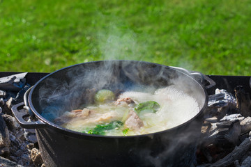 Shurpa soup in a large cast-iron cauldron outdoor. Summer food for hike.