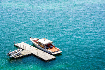 A luxury speedboat moored to an isolated, t-shape, wooden dock in green waters with an inflatable dinghy laying on the dock.