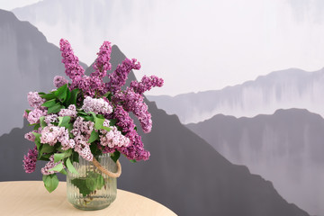 Vase with beautiful blossoming lilac on table against color background