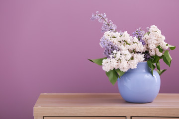 Vase with beautiful blossoming lilac on table against color background