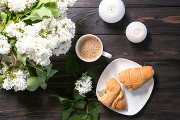 Tasty croissant with cup of coffee and beautiful blossoming lilac on table