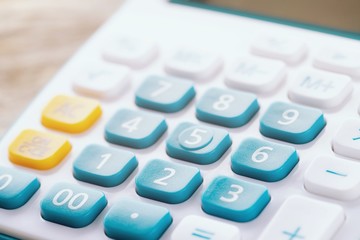 close up calculator focus at on press button keyboard. calculator colors blue yellow and white on wood table. concept calculate account finance.