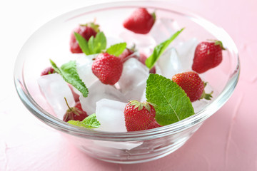 Glass bowl with ice cubes and strawberries on color background