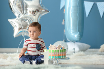 Naklejka premium Cute little boy with birthday cake sitting on fluffy rug in room