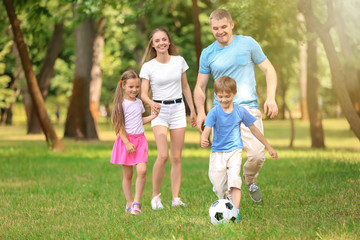 Fototapeta premium Happy family playing football in park on summer day