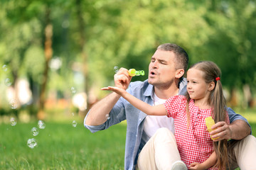 Fototapeta premium Happy father and daughter blowing soap bubbles in park