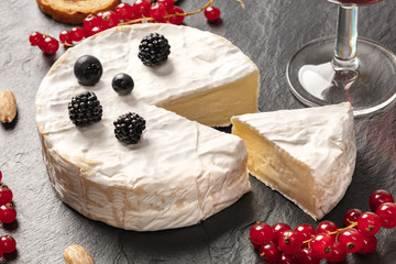 A photo of Camembert cheese with a glass of wine and fruits, on a black background