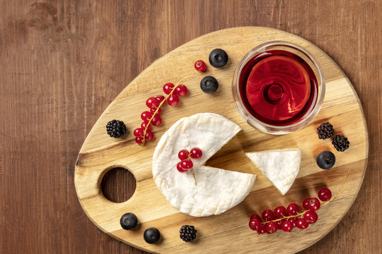 An overhead photo of Camembert cheese with a glass of red wine and fruits, on a dark rustic background with copy space