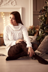 Beautiful woman sitting in the Christmas decorations in a sweater and smiling