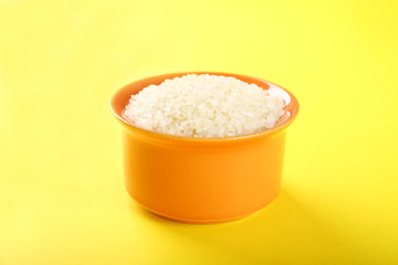 Bowl with raw rice on color background